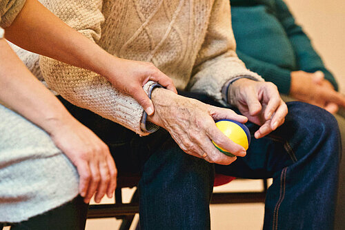 Older person holding a ball with carer supporting them